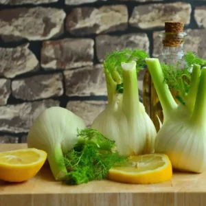 Tre finocchi freschi su un tagliere di legno con due spicchi di limone.